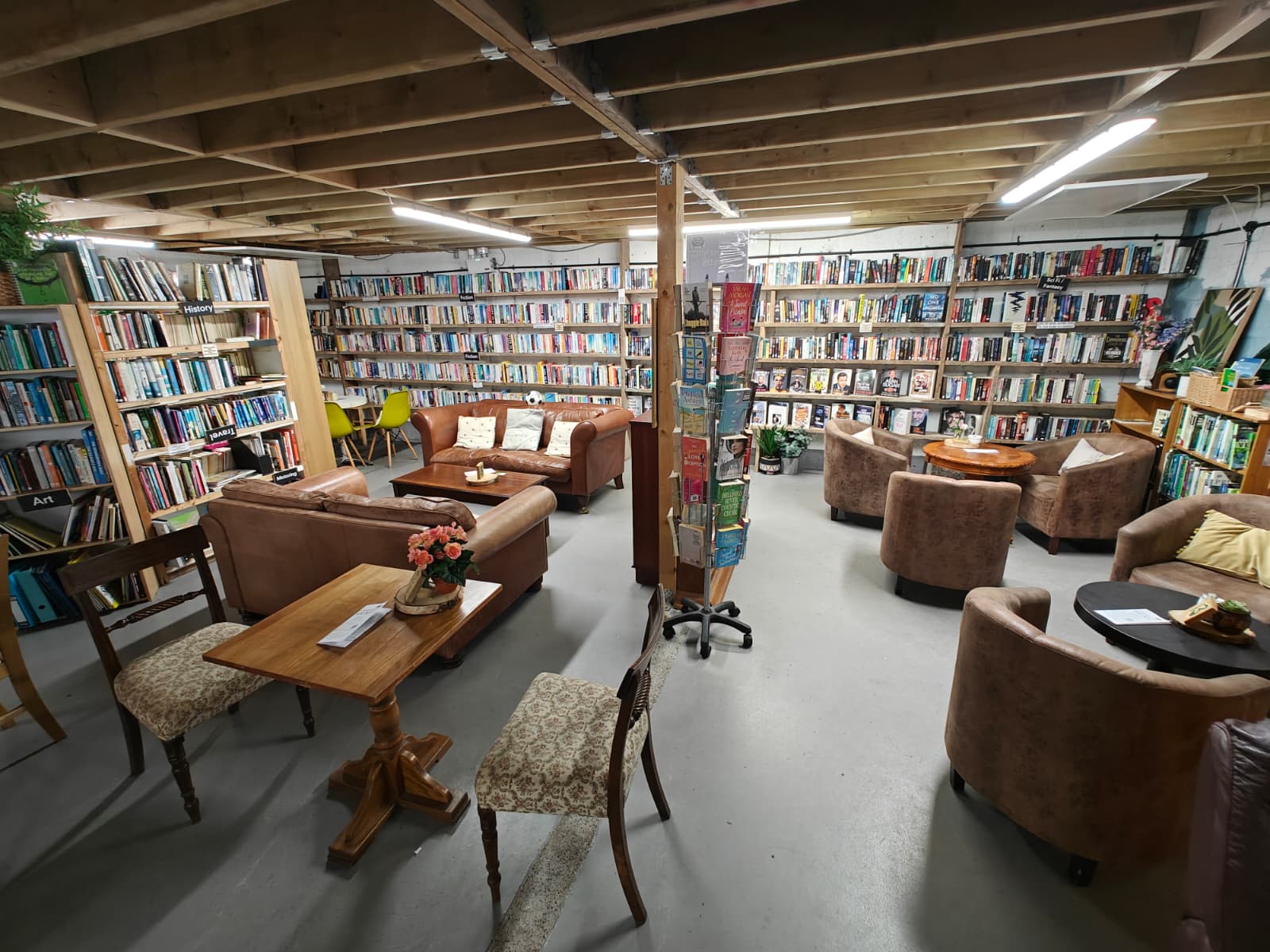 Cosy charity shop café and second-hand bookstore with shelves full of pre-loved books and vintage furniture, offering a relaxing community space.