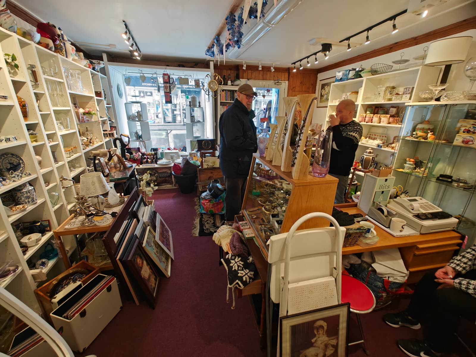 The interior of a small second-hand shop in Blairgowrie, Scotland, with a large variety of objects on shelves and laid on the floor.