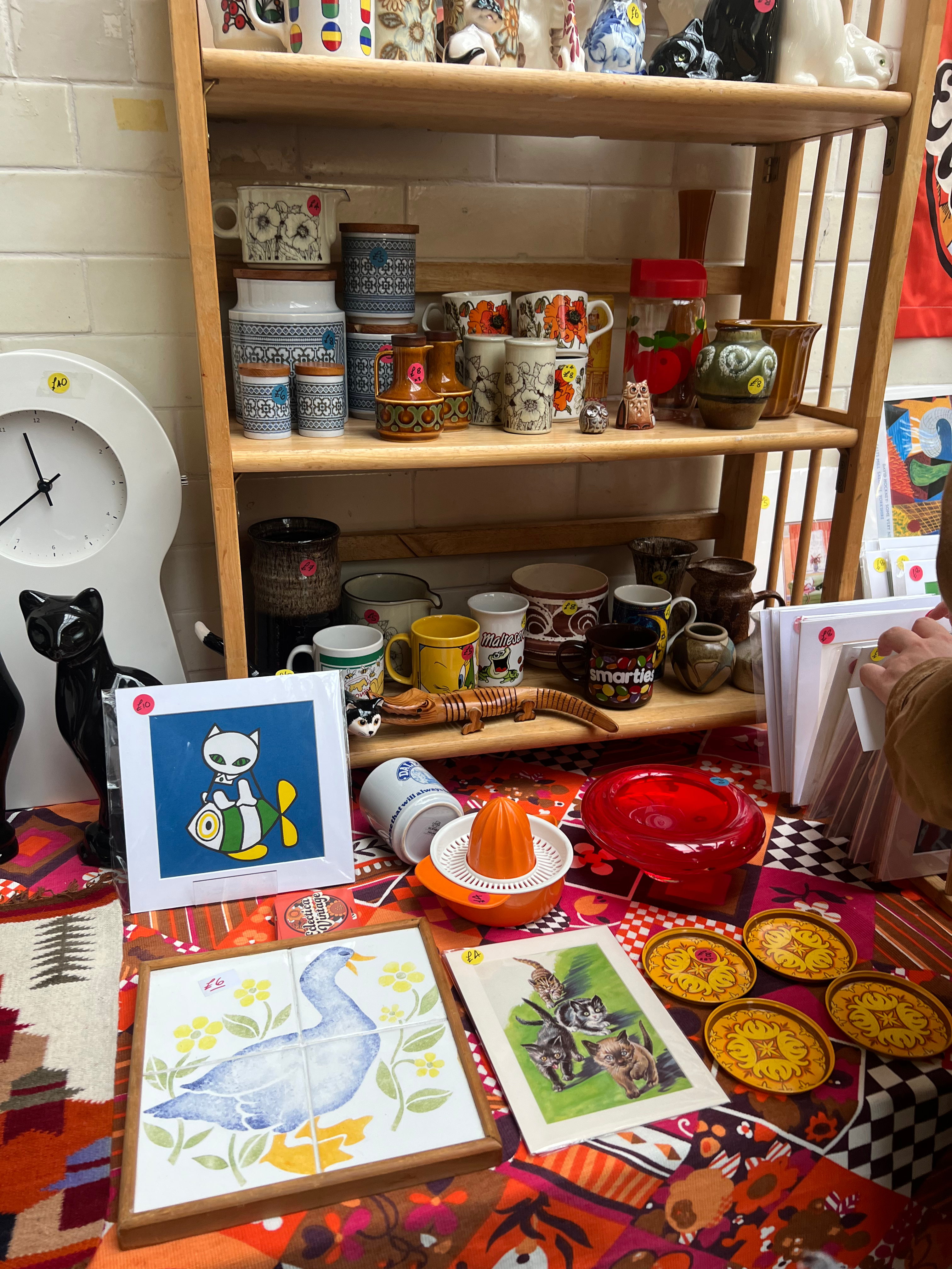 Display of vintage mugs, ceramics, retro kitchenware, and nostalgic artwork at a stall during the Vintage Home Show in Victoria Baths, Manchester, featuring 1970s patterns, novelty drinkware, and quirky animal prints.