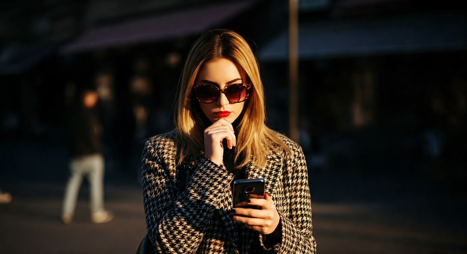 A woman wearing designer clothes looking at her phone to find sample sales online.