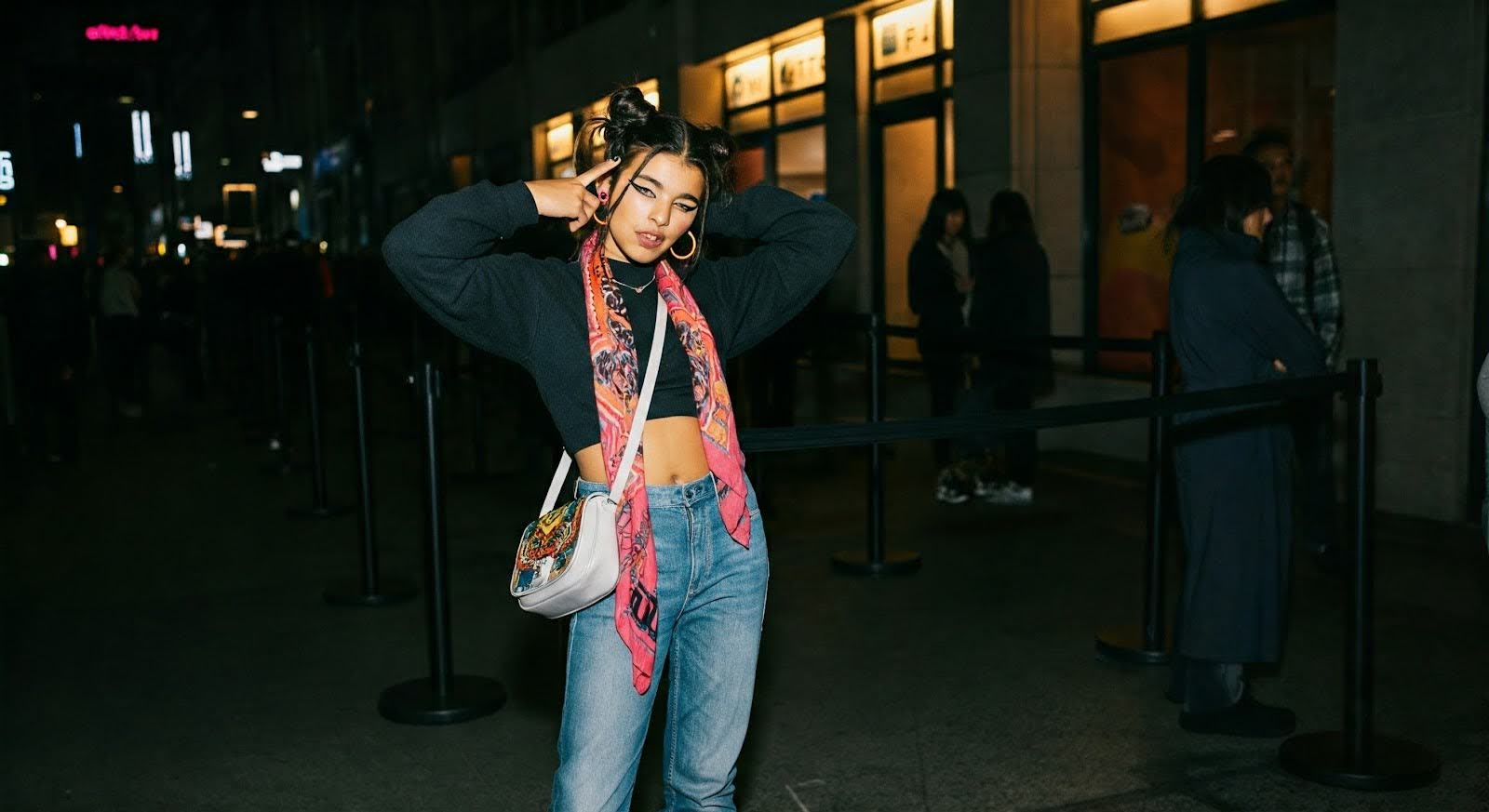 A Gen Z girl in a London queue posing with a trendy and colourful shoulder bag.