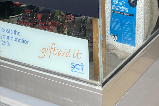A giftaid sign displayed on the window of the SCT charity shop in Brick Lane