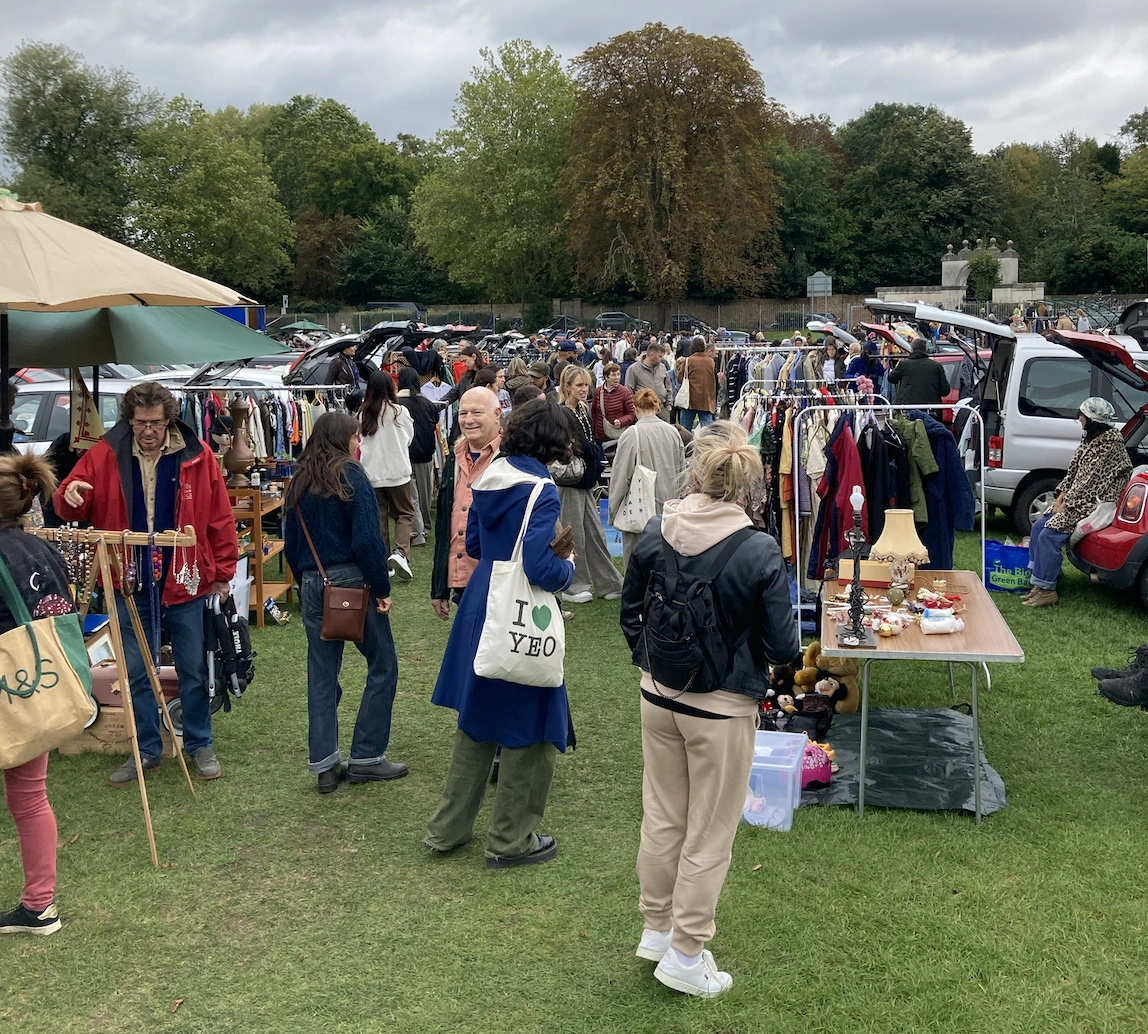 Busy Chiswick Car Boot Sale with crowds shopping for vintage clothes, antiques, and second-hand items on the outdoor field.