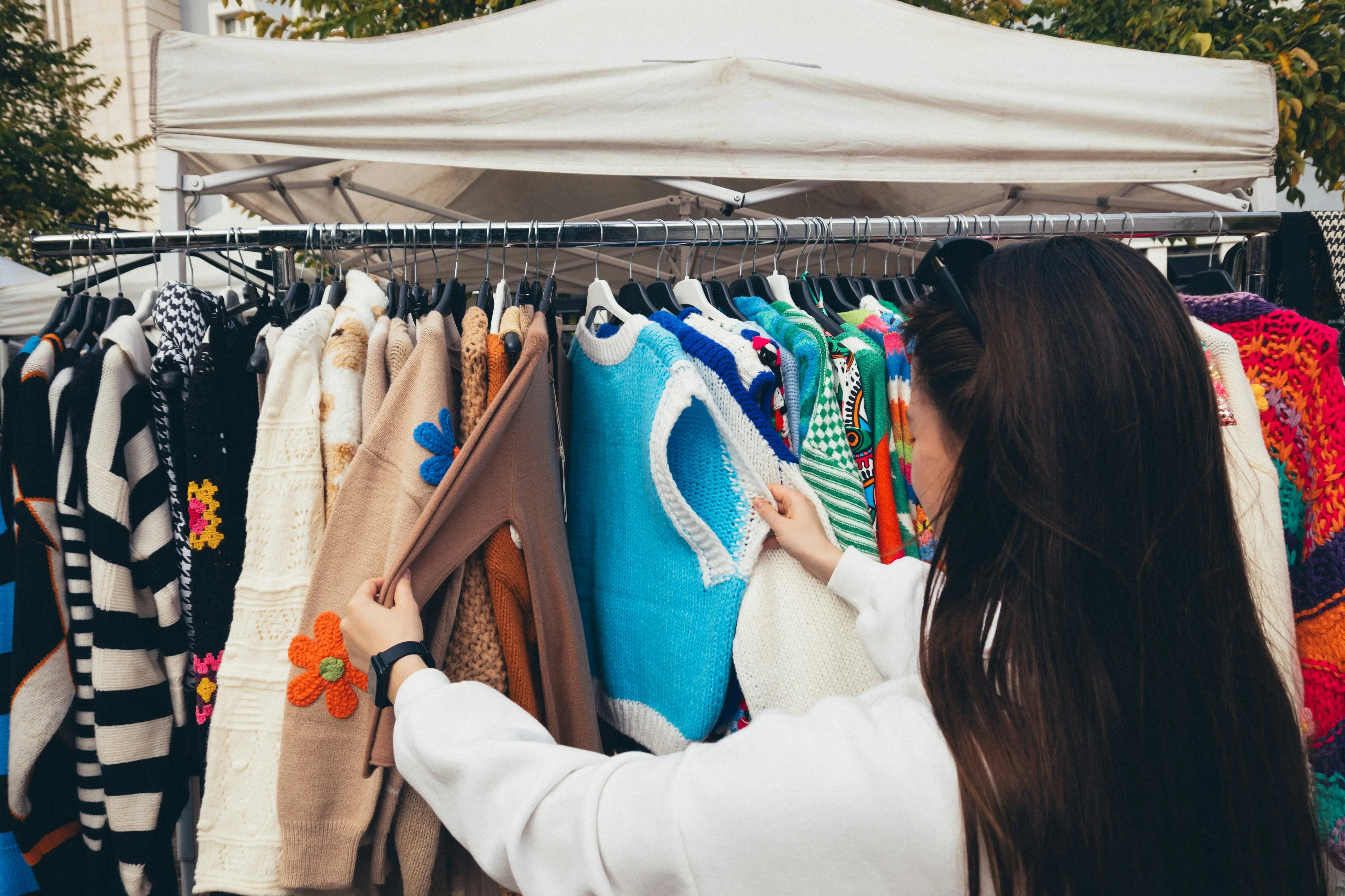 Woman browsing colourful second-hand jumpers on an outdoor charity pop-up.