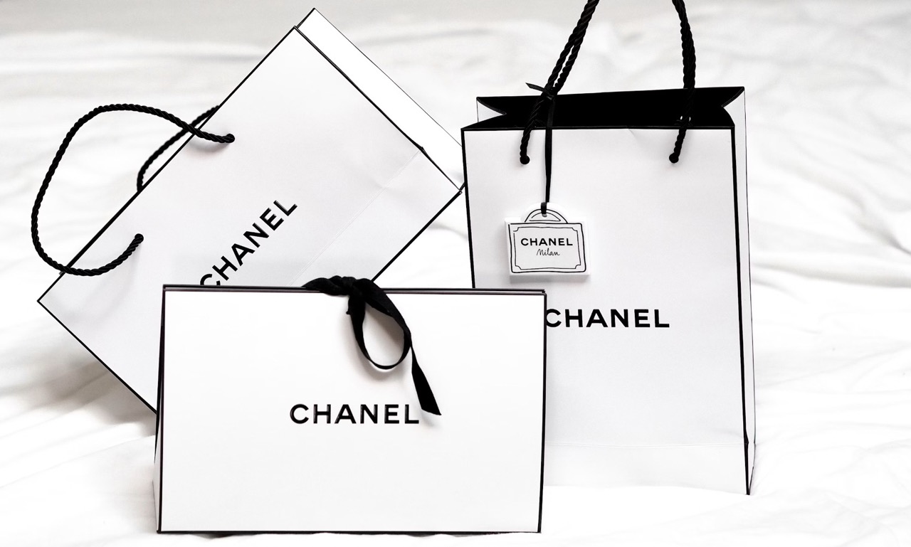 A white bed cleaning with three designer Chanel shopping bags resting at different angles