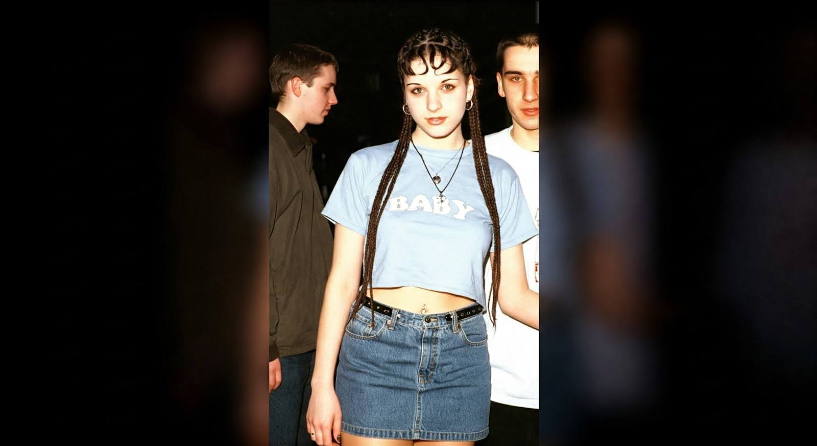 A GenZ girl with her boyfriend looks directly into the camera, wearing a low-rise Y2k look.