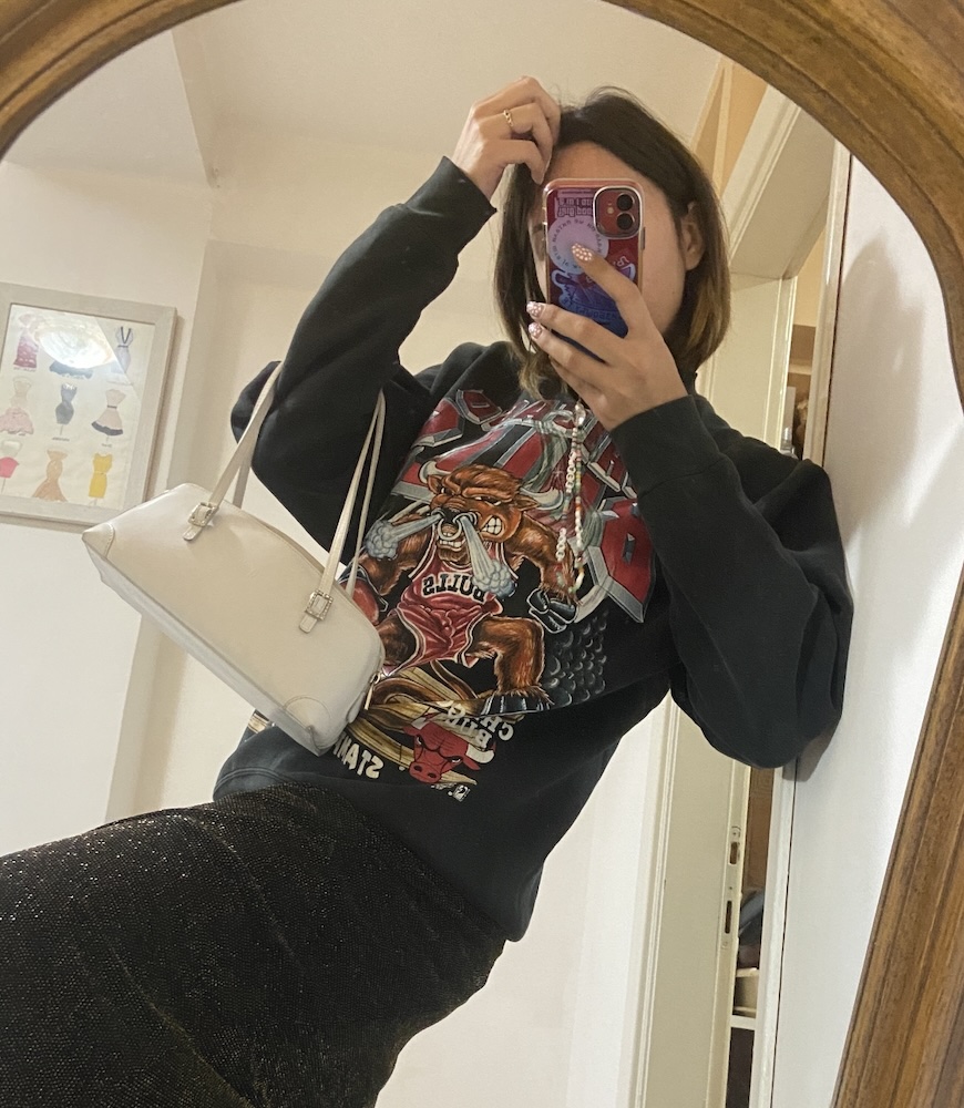 A fashionable girl pose takes a selfie in front of a mirror to show her thrifted vintage outfit.