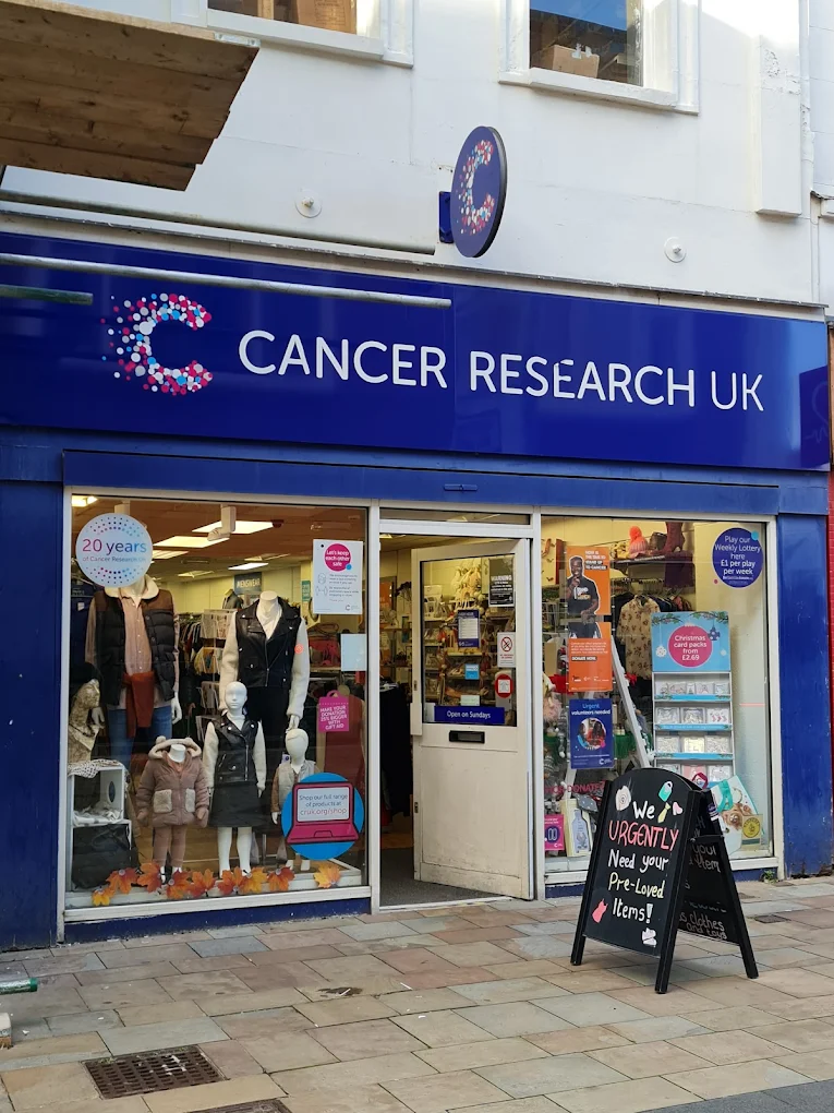 Cancer Research UK charity shop storefront with blue sign, mannequins, and pavement board