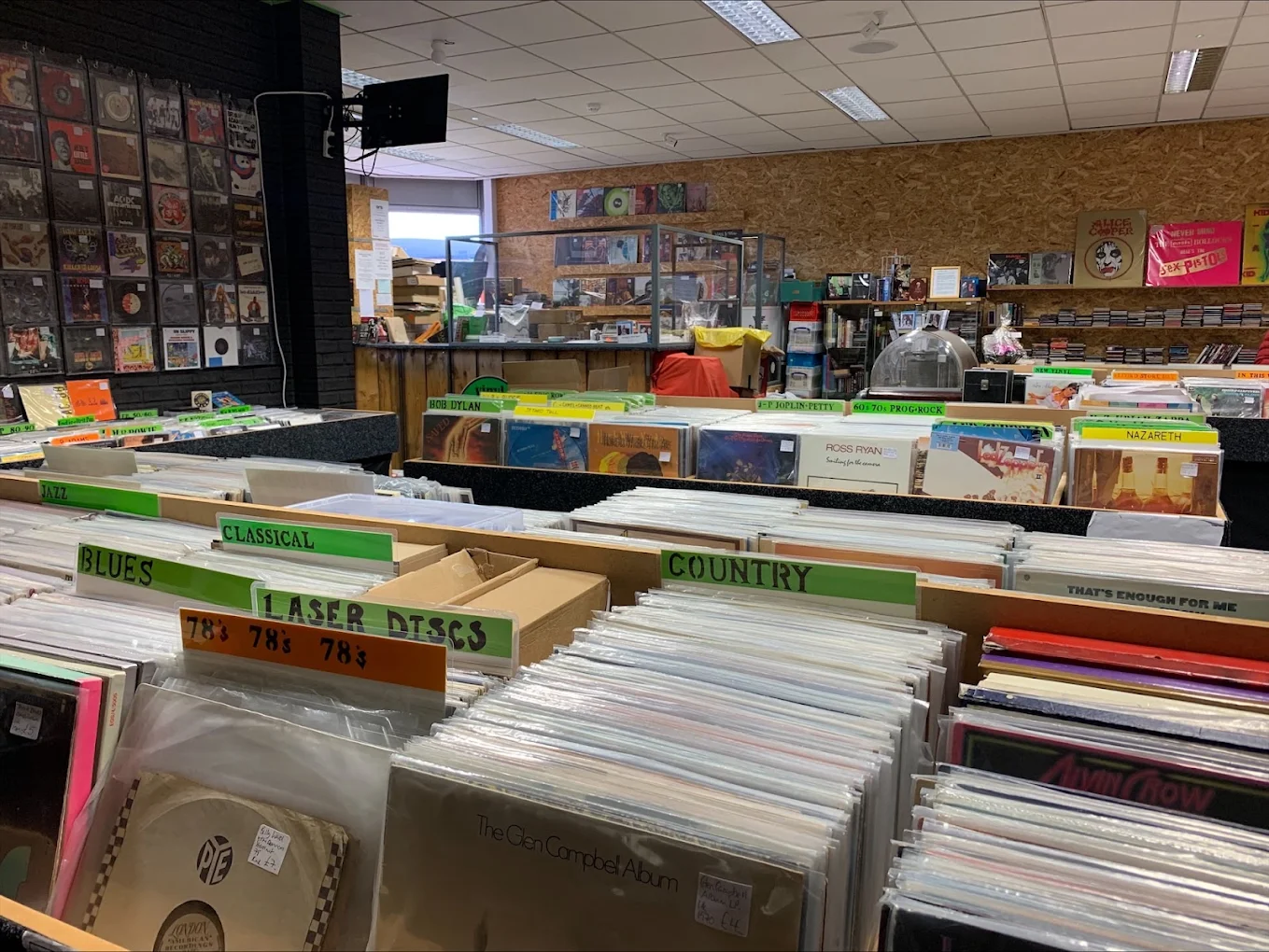 Record shop interior with vinyl bins organized by genre including jazz, blues, classical, and country