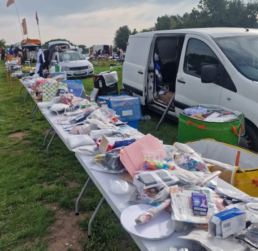 Car boot sale table of assorted household items and packaged goods next to a white van