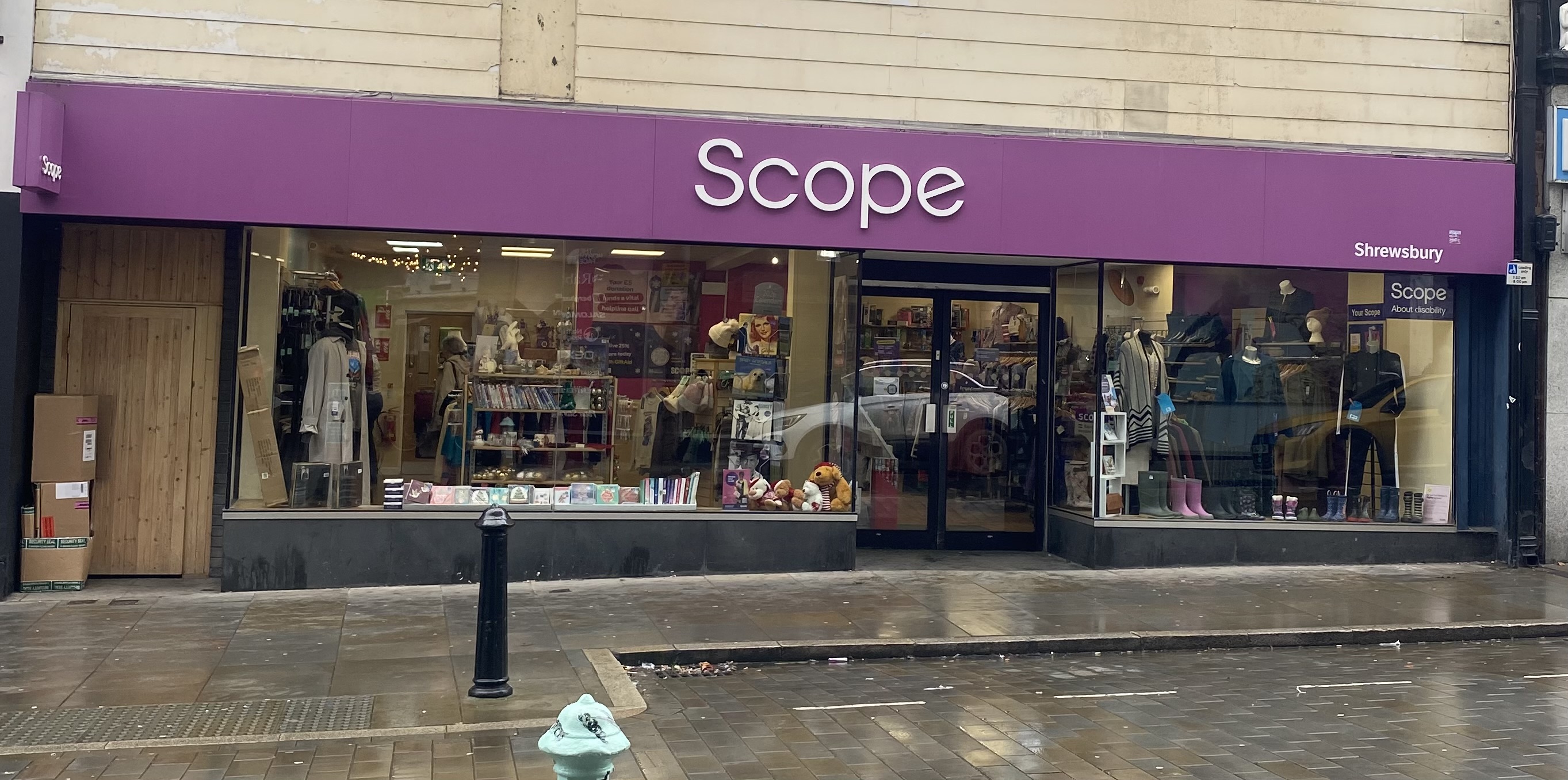 Exterior of the Scope charity shop in Shrewsbury, featuring a purple storefront and window displays of clothing, books, and donated items.