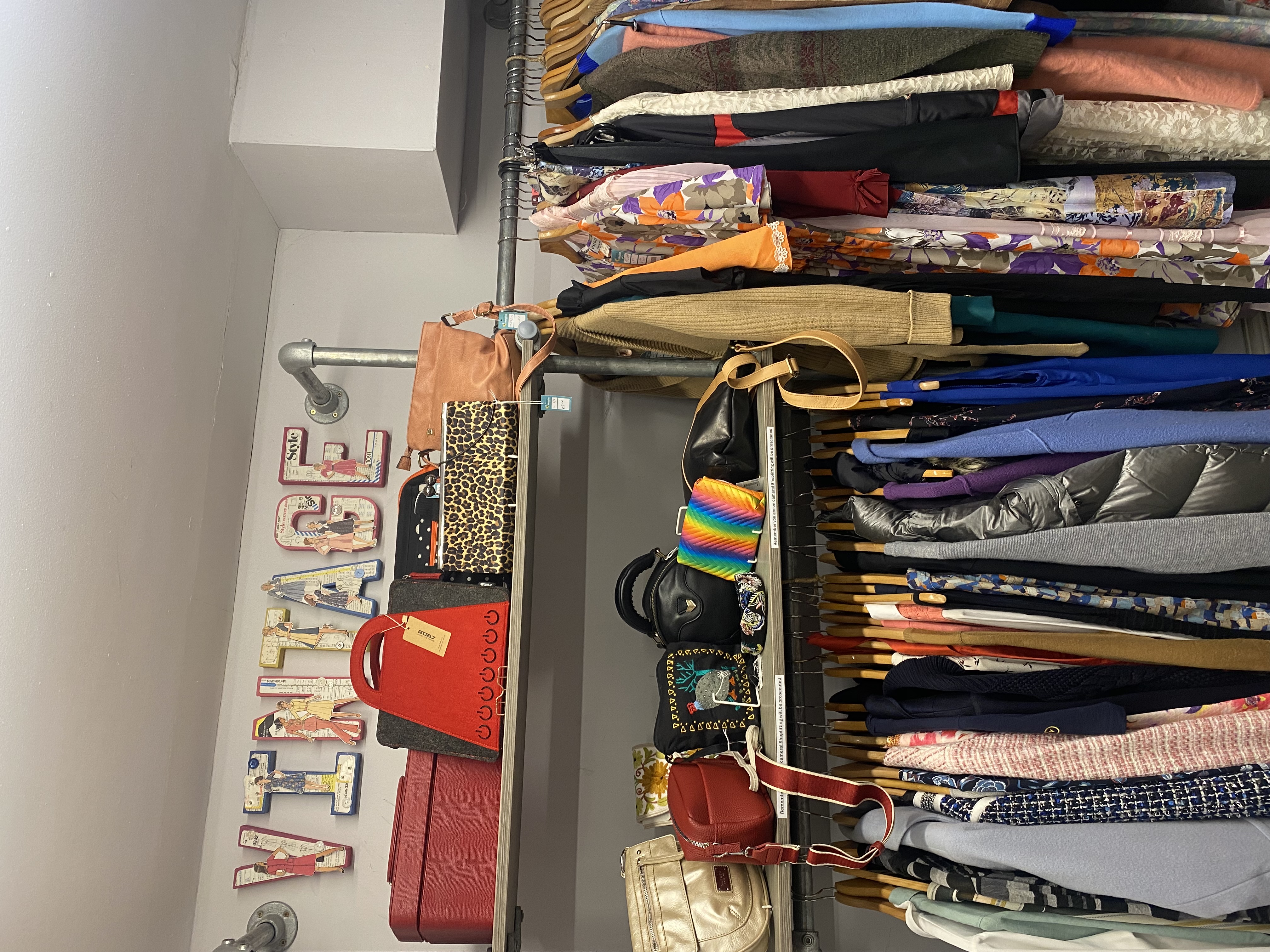 Vintage section of a charity shop in the UK featuring second-hand dresses, jackets, handbags and retro accessories displayed under a ‘Vintage’ sign.