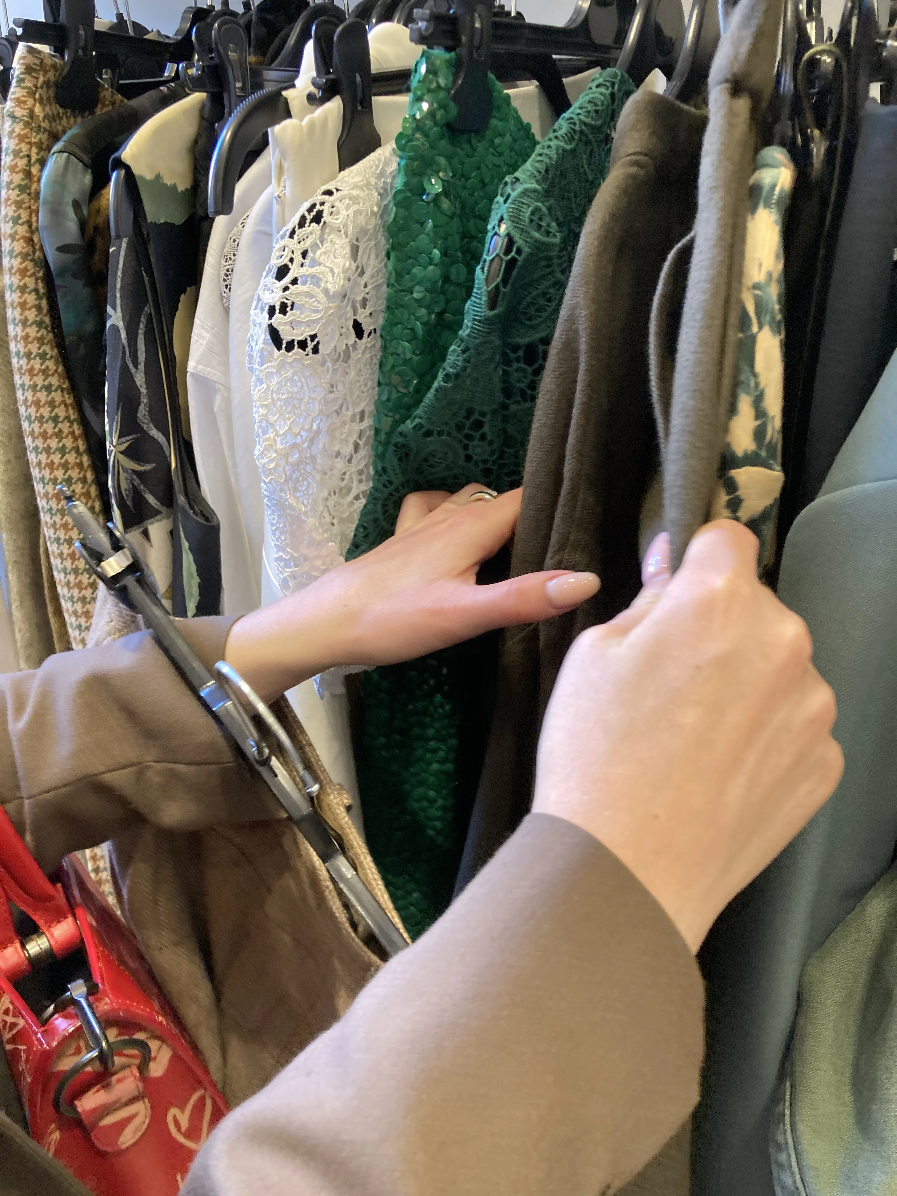 A shopper browsing vintage and second-hand clothing on a rail in a charity shop