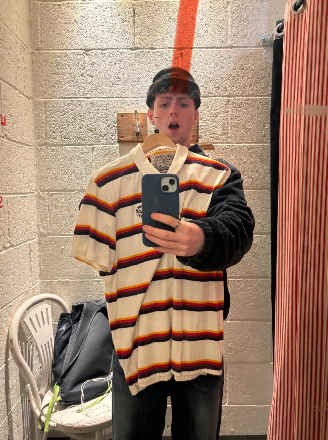 Person holding up a striped vintage polo shirt after finding it while thrifting in a second-hand shop.