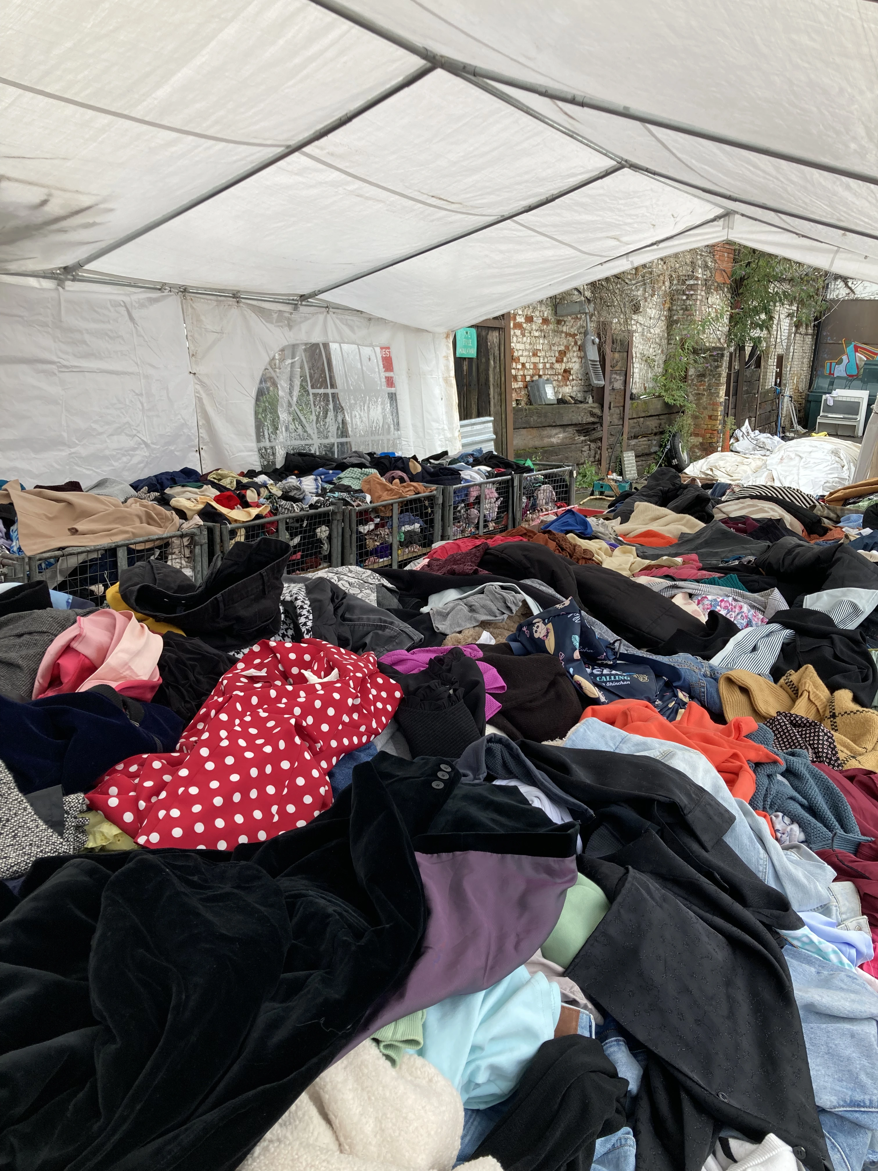 Kilo sale under a marquee with second-hand clothes piled in large bins for thrifters to sort through