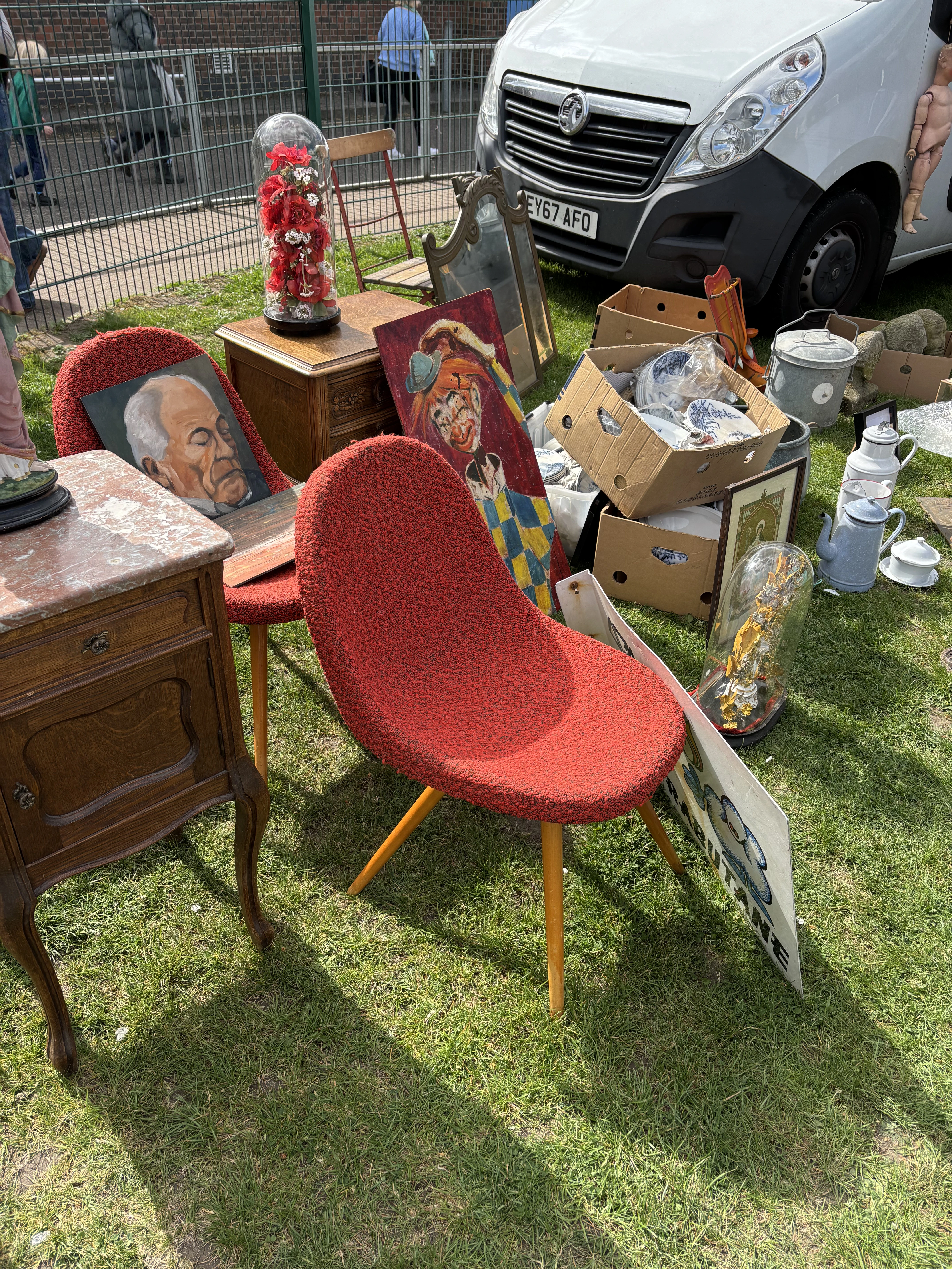 Car boot sale stall with vintage furniture, framed paintings and retro homeware laid out on the grass